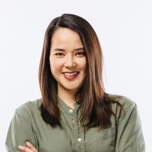 Laura is of mix ancestry, has shoulder length black hair. She smiles at the camera wearing a khaki green button up shirt