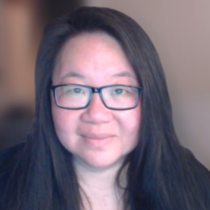 Sherry has lighter skin, long black hair, black rimmed glasses, and is looking into the camera