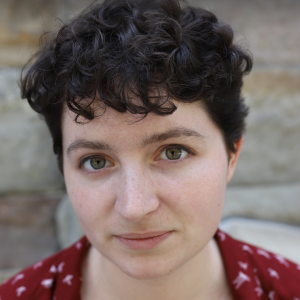 Lucy has short curly black hair, dark eyes, freckles and wears a red patterned shirt
