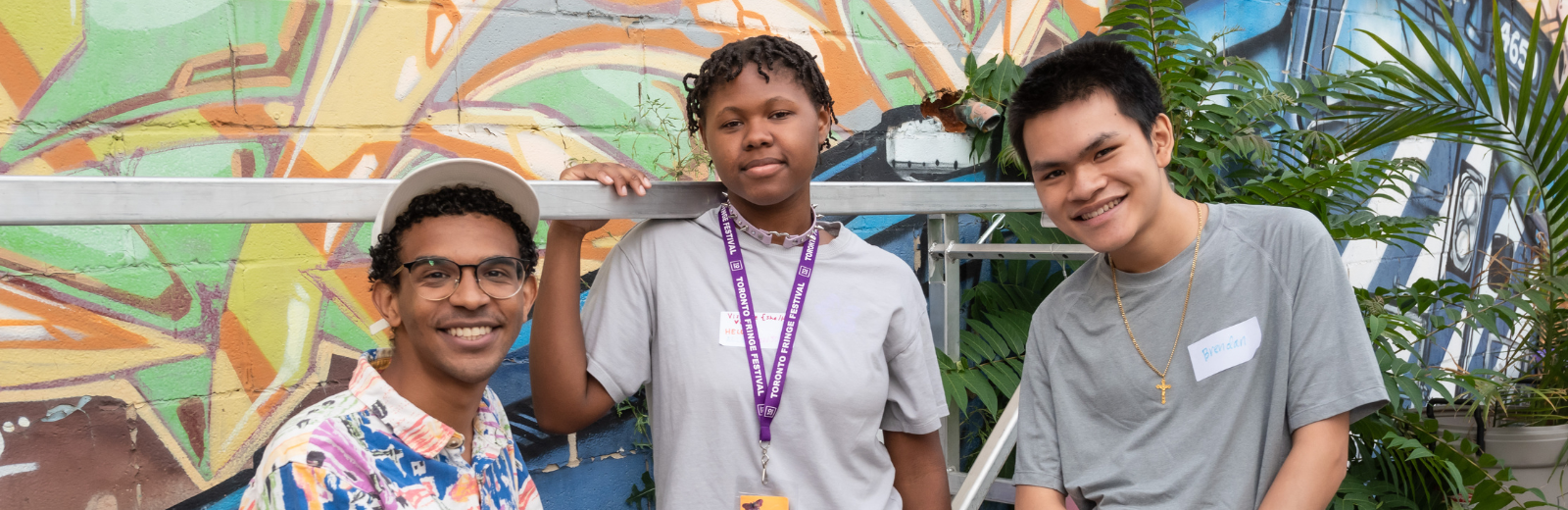 Three artists smile at the camera wearing their lanyards at the Fringe patio