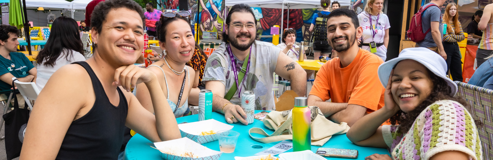 Friends sit around a table at the Fringe patio and smile at the camera